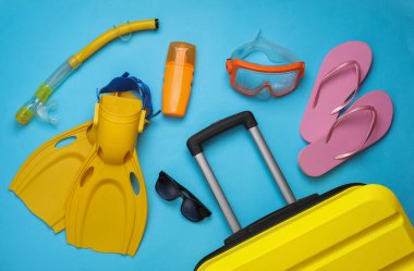 Sahil tatili, yaz tatili, taşınma konsepti. Mavi arka planda plaj aksesuarları olan bavullar. Üst Manzara. Düz yatıyordu