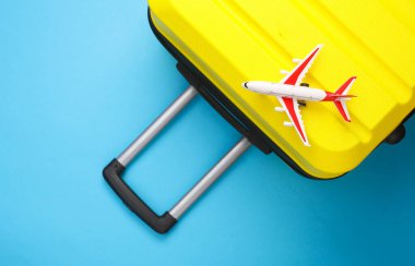 Sarı bavul, mavi arka planda oyuncak uçak valizi. Yaz tatili, seyahat, taşınma konsepti. Üst Manzara. Düz yatıyordu