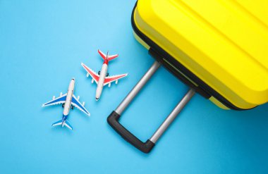 Sarı bavul, mavi arka planda oyuncak uçaklarla dolu bavul. Yaz tatili, seyahat, taşınma konsepti. Üst Manzara. Düz yatıyordu