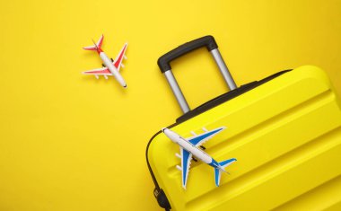 Sarı bavul, sarı arka planda oyuncak uçaklarla dolu bavul. Yaz tatili, seyahat, taşınma konsepti. Üst Manzara. Düz yatıyordu