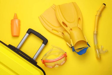 Sahil tatili, yaz tatili, taşınma konsepti. Plaj aksesuarlı bavullar: dalış maskesi, paletler ve sarı arka planda şnorkel. Üst Manzara. Düz yatıyordu