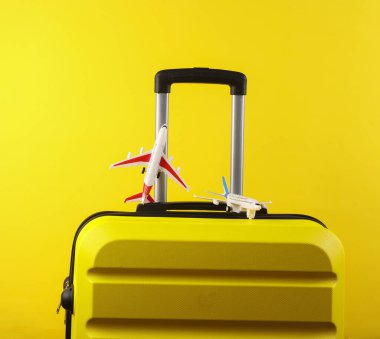 Sarı plastik çanta ve sarı arka planda oyuncak uçak. Bagaj, turizm, tatil, taşınma konsepti