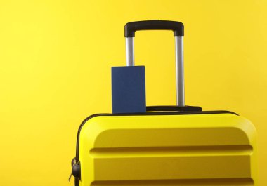 Sarı arka planda pasaportu olan sarı plastik bir valiz. Bagaj, turizm, tatil, taşınma konsepti