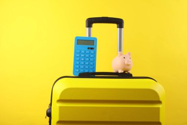 Sarı plastik çanta, kumbaralı, hesap makinesi ve sarı arka plan. Tatil bütçesi
