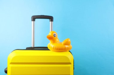 Mavi arka planda şişme ördek olan sarı plastik bir valiz. Yaz tatili, turizm, tatil, taşınma konsepti
