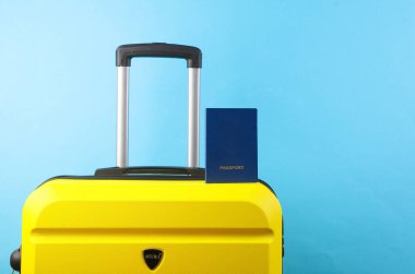 Mavi arka planda pasaportu olan sarı plastik bir valiz. Bagaj, turizm, tatil, taşınma konsepti