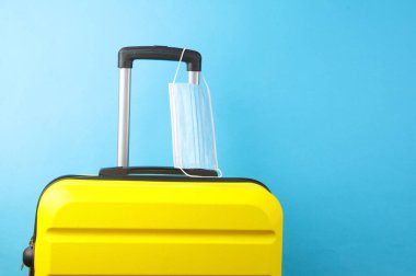 Mavi arka planda tıbbi maskesi olan bir valiz. Karantina, covid 19, seyahat kuralları