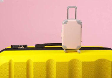 Sarı plastik valiz ve pembe arka planda minyatür. Bagaj, turizm, tatil, taşınma konsepti