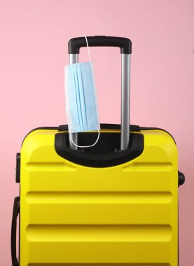 Pembe arka planda tıbbi maskeli valiz. Karantina, covid 19, aşı, seyahat kuralları