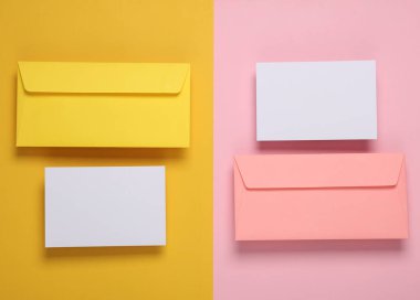 Renkli arkaplanda beyaz boş tebrik kartları olan pembe ve sarı zarflar.