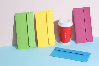 Renkli zarflar ve pastel parlak arka planda kağıt kahve fincanı olan yaratıcı bir düzen. Minimalizm