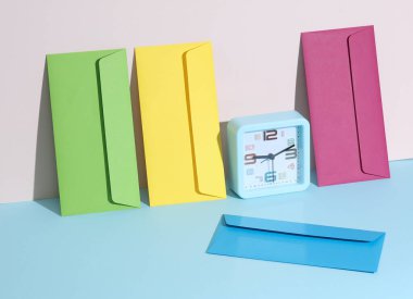 Renkli zarflar ve pastel parlak arkaplan üzerindeki saat ile yaratıcı bir düzen. Minimalizm