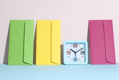 Renkli zarflar ve pastel parlak arkaplan üzerindeki saat ile yaratıcı bir düzen. Minimalizm