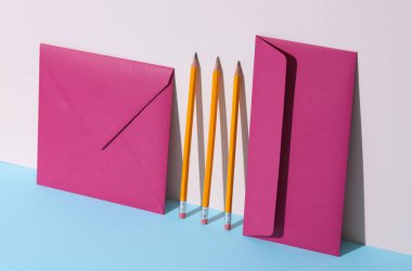 Mor zarflar ve pastel arka planda gölgeli kalemler. Minimalizm, yaratıcı düzen