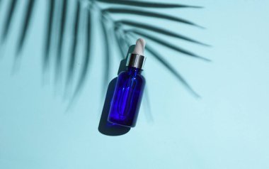 Mavi arka planda serum şişesi ve palmiye yaprağı gölgesi. Yaratıcı güzellik düzeni. Üst görünüm.