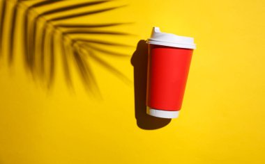 Marka modeli. Sarı arka planda palmiye yaprakları olan kırmızı karton bardak.