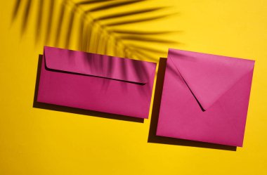 Sarı arka planda iki mor zarf ve palmiye yaprağı gölgesi. Minimum yaz konsepti. Üst görünüm