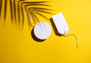 İp üzerinde beyaz fiyat etiketleri ve sarı arka planda palmiye yaprağı gölgesi. Satış, alışveriş konsepti