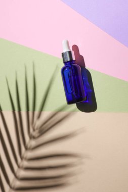 Pastel arka planda serum şişesi ve palmiye yaprağı gölgesi. Yaratıcı güzellik düzeni. Üst görünüm.