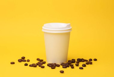 Kapaklı beyaz kahve fincanı ve sarı arka planda kahve çekirdekleri.