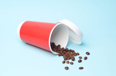 Mavi arka planda kahve çekirdekleri olan kırmızı kahve fincanı.