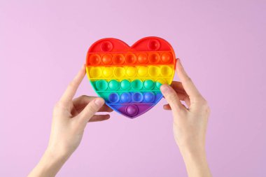 Eller tutarken kalp şeklinde, gökkuşağı rengi mor arka planda.