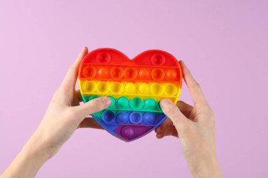 Eller tutarken kalp şeklinde, gökkuşağı rengi mor arka planda.