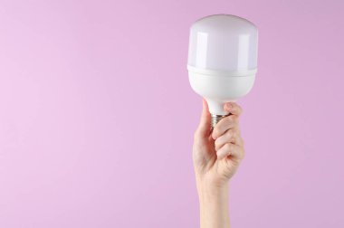 Mor arka planda büyük bir ampulü tutan el.