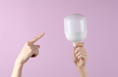 Mor arka planda büyük bir ampulü tutan el.