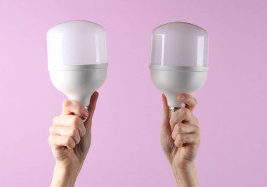 Elektrik tasarrufu. Mor arka planda iki tane kurşun ampul tutan eller.