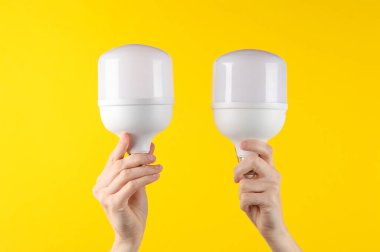 Elektrik tasarrufu. Sarı arka planda kurşun ampulleri tutan eller