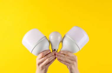 Elektrik tasarrufu. Sarı arka planda kurşun ampulleri tutan eller
