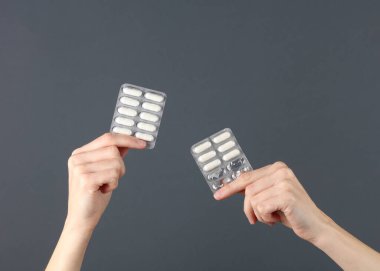Koyu gri arka planda hapların kabarcıklarını tutan eller.
