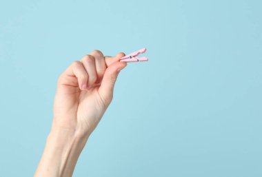 Mavi arka planda pembe bir mandal tutan bir kadın.