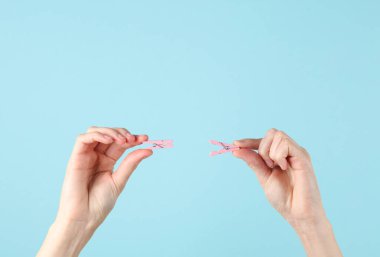 Kadın eli mavi arka planda iki tane pembe tahta mandal tutar.