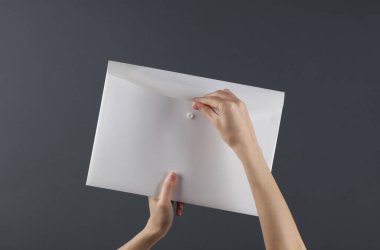Kadın elleri, arka planda beyaz plastik bir zarf klasörünü açıyor. İş konsepti