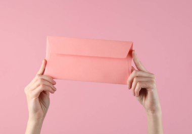 Pembe pastel arka planda pembe bir zarf tutan kadın eller.