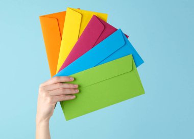 Kadının elinde mavi bir arka planda renkli zarflar var.