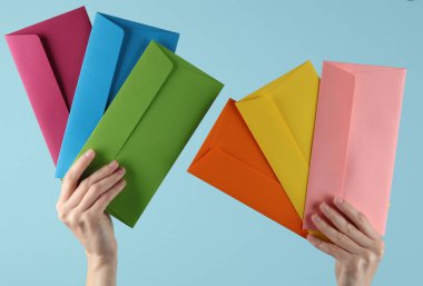 Mavi arka planda renkli zarfları tutan kadın elleri