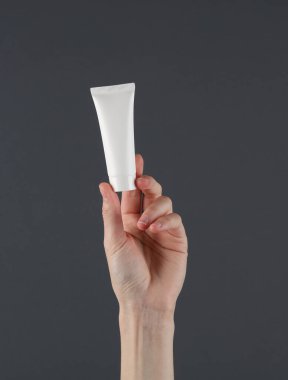 Kadınlar beyaz krema tüpünü koyu arka planda tutarlar. Güzellik modeli.