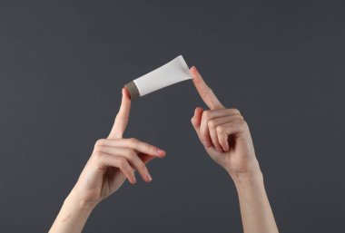 Kadınların elleri arka planda beyaz krema tüpü tutuyor. Güzellik modeli.