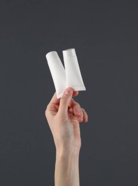 Kadın eli, arka planda beyaz krema tüplerini tutuyor. Güzellik konsepti. Modelleme. Tasarım şablonu