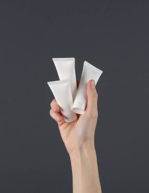 Kadın eli, arka planda beyaz krema tüplerini tutuyor. Güzellik konsepti. Modelleme. Tasarım şablonu
