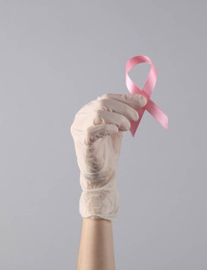 Tıbbi eldivenin içinde pembe meme kanseri farkındalığı kurdelesi var.