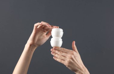 Eller koyu gri arka planda beyaz krema kavanozlarını tutar. Model, tasarım şablonu, güzellik konsepti