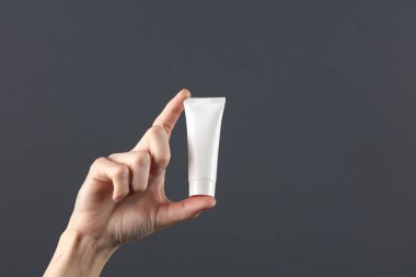 Kadının eli koyu gri arka planda beyaz krema tüpünü tutuyor. Tasarım için şablon, yaratıcı güzellik modeli