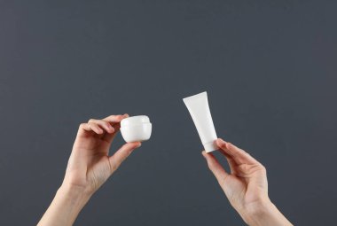 Kadının elleri beyaz krema tüpü ve koyu gri arka planda kavanozlar tutuyor. Tasarım için şablon, yaratıcı güzellik modeli