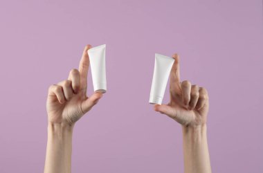 Mor arka planda beyaz krema tüpleri tutan kadın eller. Tasarım şablonu, yaratıcı güzellik modeli. Cilt bakımı