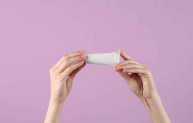 Mor arka planda beyaz krema tüpü tutan kadın eller. Tasarım şablonu, yaratıcı güzellik modeli. Cilt bakımı