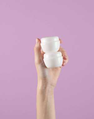 Koyu gri arka planda beyaz krema kavanozları tutuyordu. Model, tasarım şablonu, güzellik konsepti, cilt bakımı